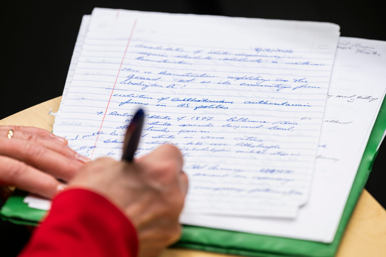 Close-up of a person taking handwritten notes with a pen on lined paper during a lecture.